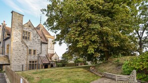 A stone building with a grassy courtyard, a wooden bench, and a large tree. - 3 Coram Tower (Lyme Regis)