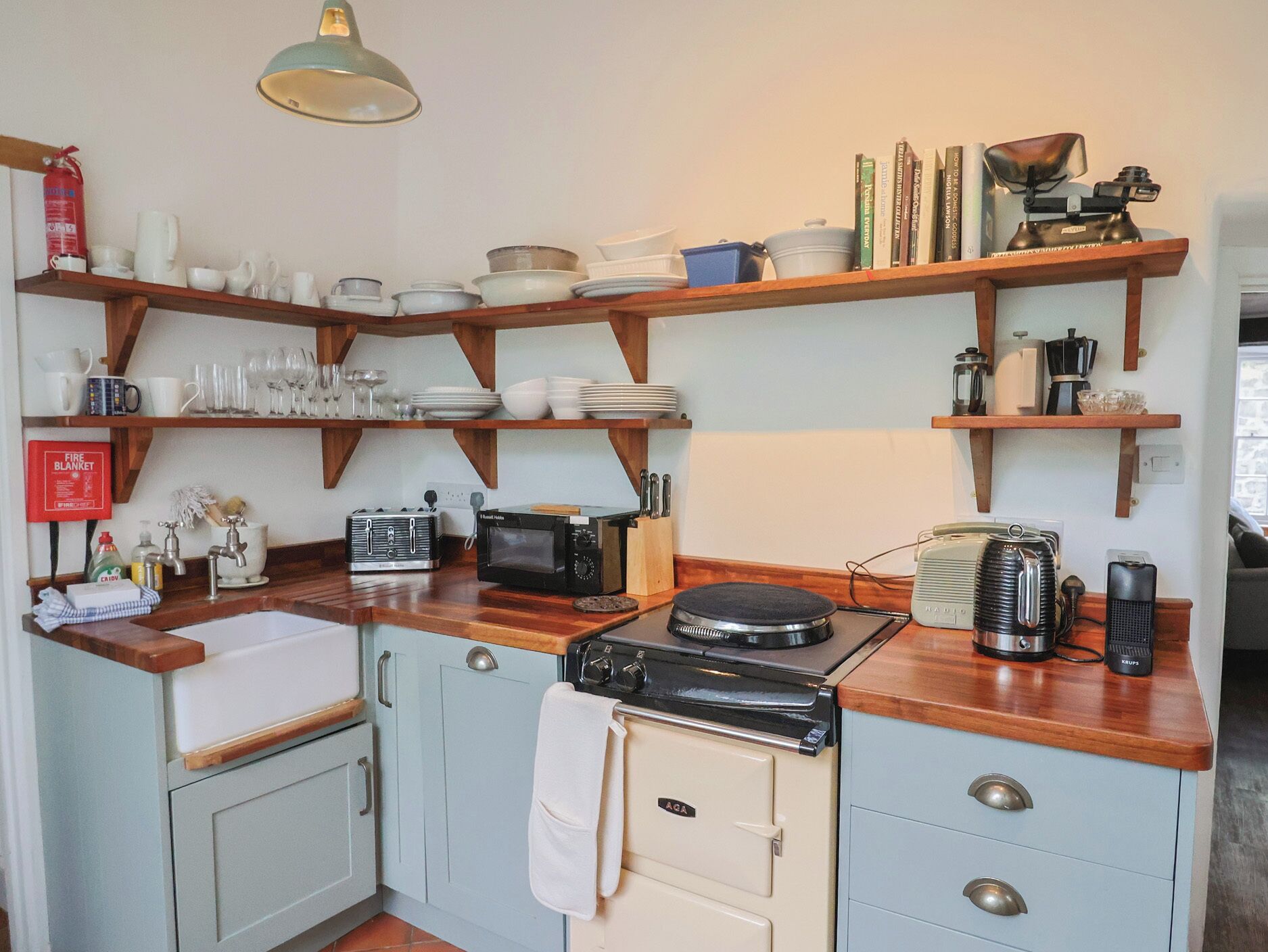 A kitchen with wooden shelves, a microwave, a toaster, a kettle, and a vintage radio.