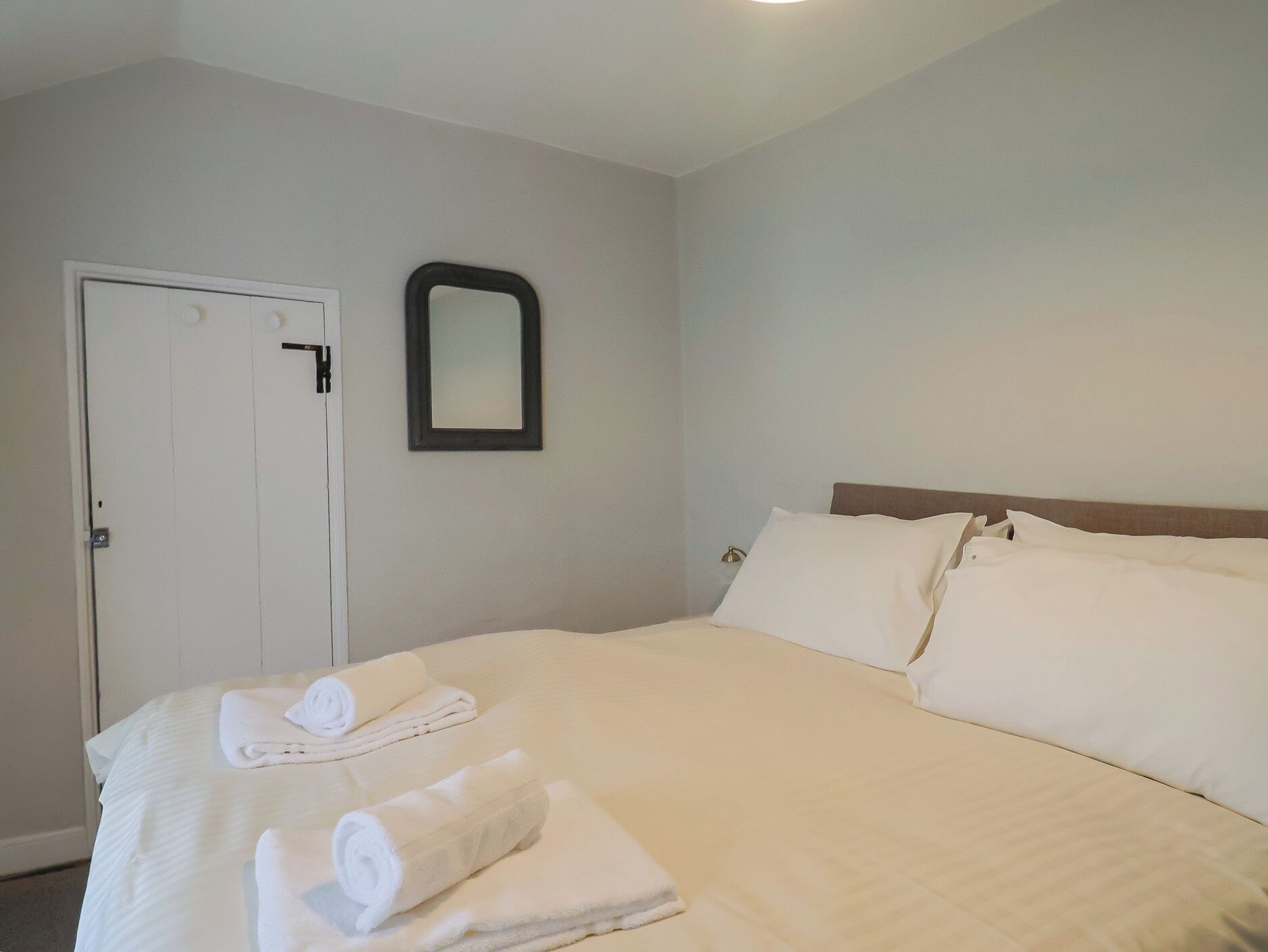 A hotel room with a bed, white towels, a door, and a mirror on the wall.