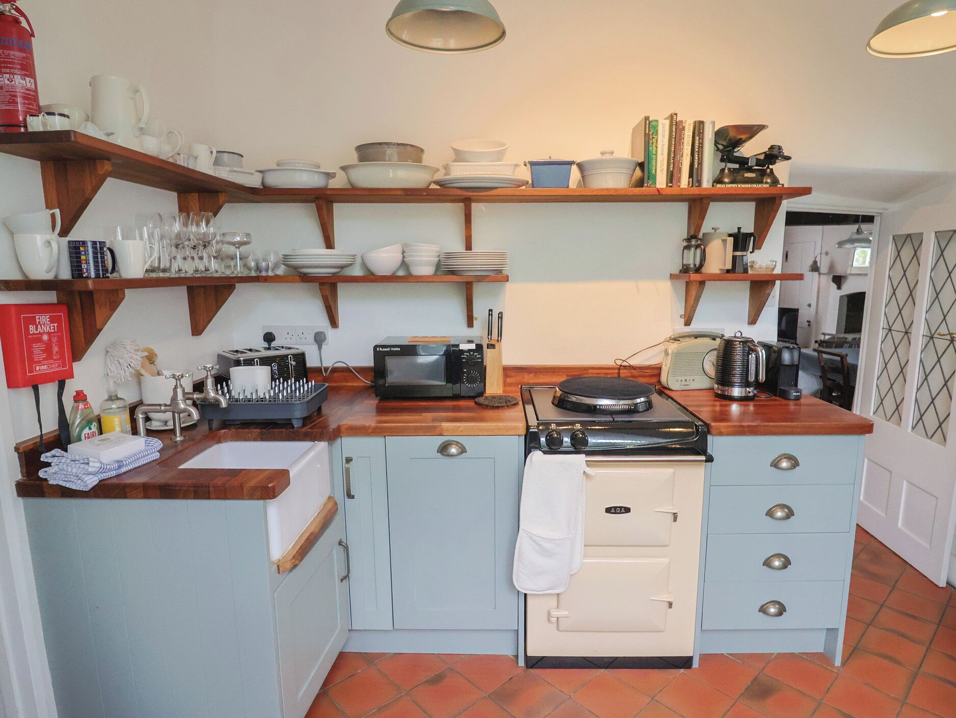 A kitchen with a stove, microwave, and various kitchenware on shelves.
