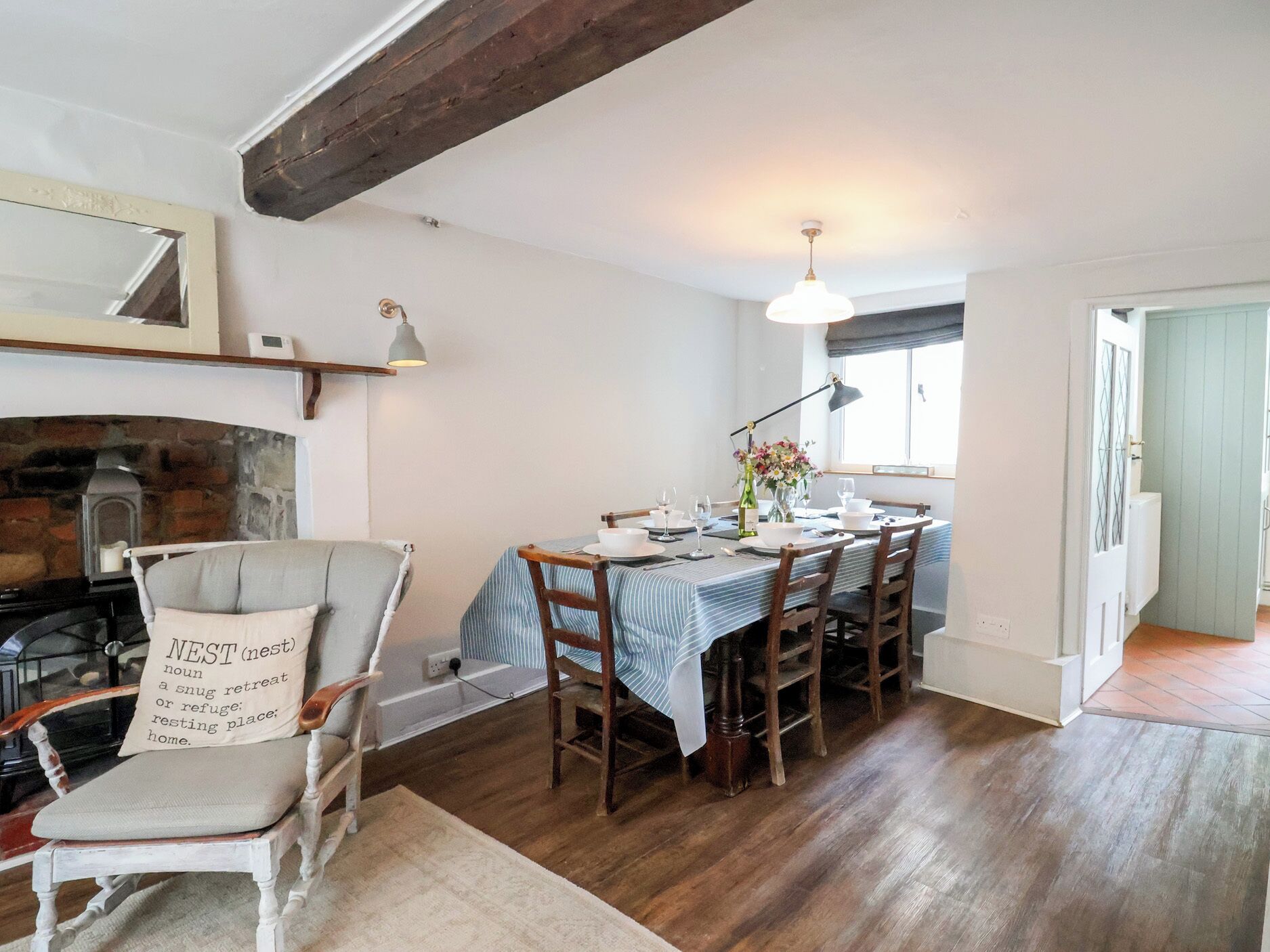 Un coin repas avec une table dressée pour quatre personnes, une cheminée, un fauteuil avec un coussin et un luminaire suspendu.