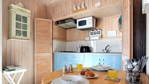 Une cuisine en bois équipée d’un four à micro-ondes, d’une machine à café et d’une table à manger, cette dernière étant dressée avec des assiettes, un bol et un verre de jus de fruits.