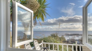 Un balcon avec vue sur la mer, un palmier et une balustrade blanche.