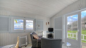 Une pièce comprenant un lit, un canapé gris, une petite table, un radiateur et un téléviseur posé sur une étagère.
