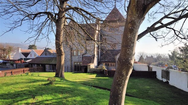 Une cour avec un grand arbre, un bâtiment en pierre doté d’un toit conique et un mur en briques.