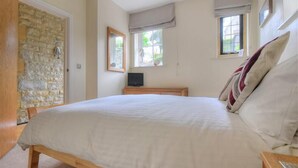 Une chambre à coucher avec un lit, un mur en pierre, une fenêtre et un téléviseur.