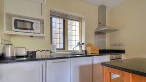 Une cuisine avec des meubles blancs, un four à micro-ondes, une cuisinière et une fenêtre avec des stores.