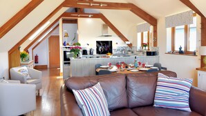 A spacious loft with a high ceiling, exposed wooden beams, a kitchen with modern appliances, and a leather sofa with striped pillows. - Bucket & Spade (Lyme Regis)