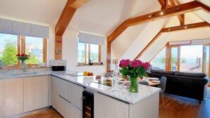 A modern kitchen with wooden beams, large windows, and a view of the outdoors. - Bucket & Spade (Lyme Regis)