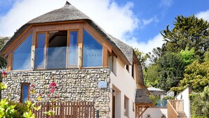 A two-story house with a stone facade, large windows, and a thatched roof. - Bucket & Spade (Lyme Regis)