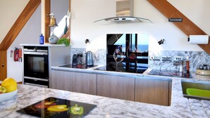 A modern kitchen with a large island, built-in oven, and a view of the sea. - Bucket & Spade (Lyme Regis)