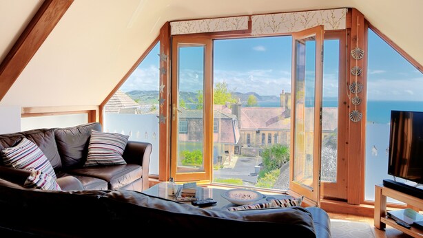 A cozy room with a large window, a sofa, and a television. - Bucket & Spade (Lyme Regis)