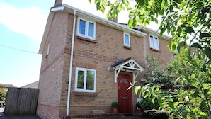 A two-story brick house with a red door, white-framed windows, and a small porch. - 1 Coppers Knapp (Lyme Regis)