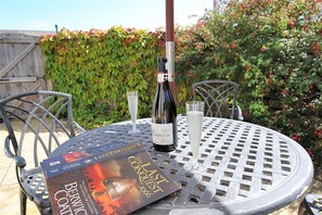 Une table ronde en métal, avec une bouteille de vin et deux verres, un livre intitulé « La dernière conquête, 1066 » posé dessus, et une chaise en métal.