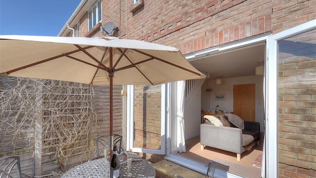 A patio with a table and chairs, a bottle of wine, and a large umbrella. - 1 Coppers Knapp (Lyme Regis)