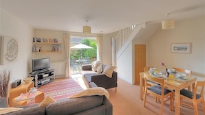 A living room with a sofa, TV, bookshelf, dining table, and chairs. There is a staircase leading to another level. - 1 Coppers Knapp (Lyme Regis)