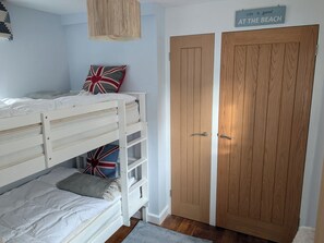 A bedroom with a bunk bed, a wooden wardrobe, and a sign that reads 'Life is good at the beach.'
