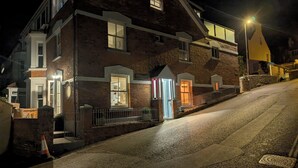 Un bâtiment à deux étages avec une façade en briques, une entrée fermée par un portail et un petit espace porche.