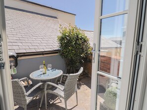 Eine Terrasse mit einem runden Tisch, Korbstühlen, einer Weinflasche und einem kleinen Baum.