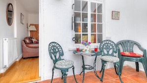 A cozy room with a wooden floor, a white wall, a window with white shutters, and a table with chairs. - Windwhistle (Lyme Regis)