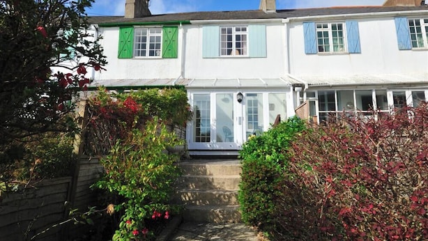 A traditional white building with green shutters, a visible front door, and a small garden area with red flowers and shrubs. - Windwhistle (Lyme Regis)