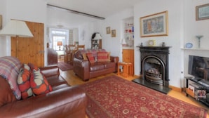 A living room with a fireplace, leather sofa, and a red patterned rug. - Windwhistle (Lyme Regis)
