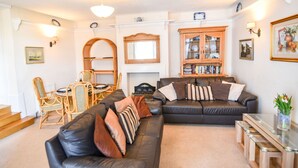 A living room with a fireplace, two leather sofas, a dining table with chairs, and a bookshelf. - Okanagan (Lyme Regis)