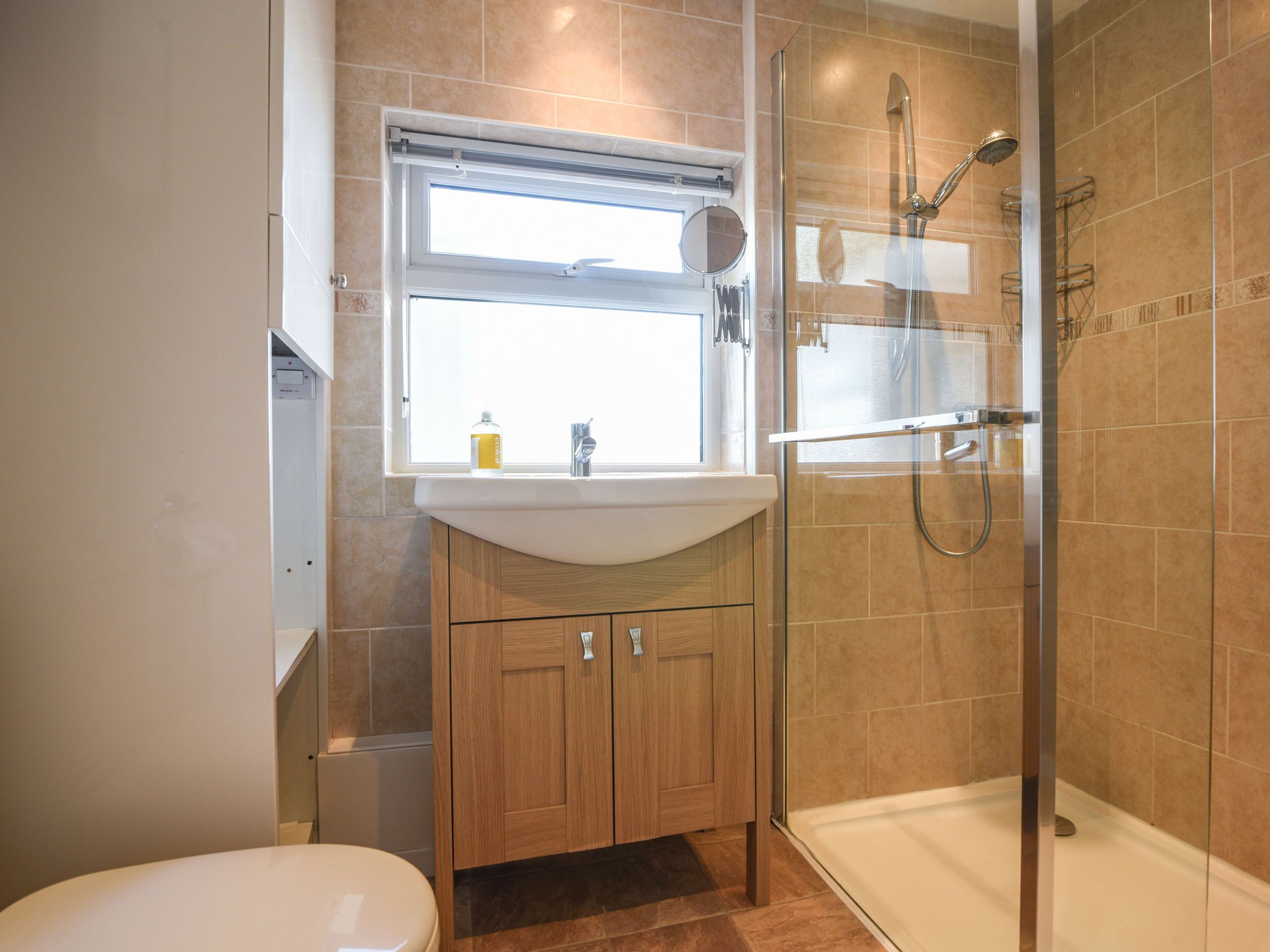 Ein modernes Badezimmer mit einer gläsernen Duschkabine, einem weißen Waschbecken und Holzschränken.