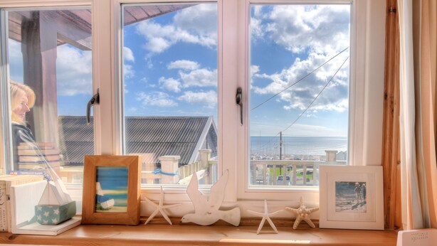 Una habitación con vistas al mar a través de amplios ventanales, una mesa de madera y varias fotografías enmarcadas y decoraciones con estrellas de mar.