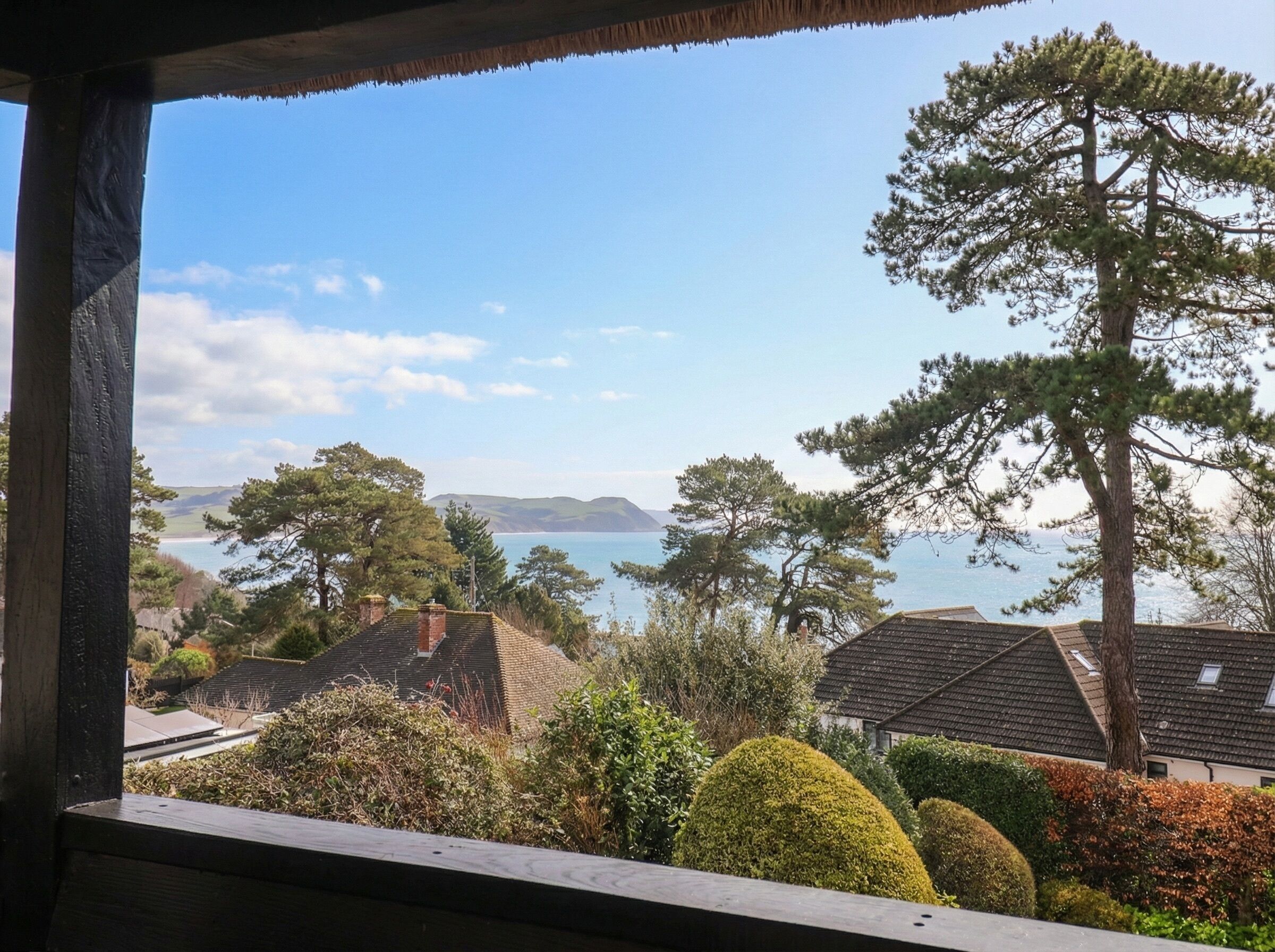 Uitzicht op de kust vanuit een raam, met huizen en bomen op de voorgrond.