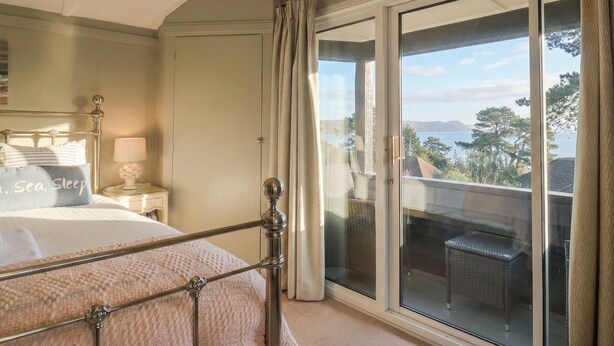 A bedroom with a bed, a nightstand, a lamp, and a view of the outdoors through a sliding glass door. - Maries (Lyme Regis)