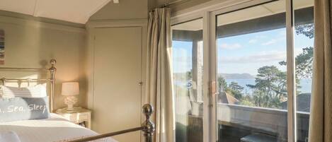 A bedroom with a bed, a nightstand, a lamp, and a view of the outdoors through a sliding glass door.