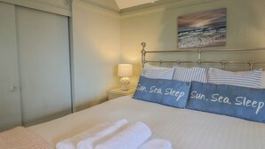 A neatly made bed with rolled white towels, a bedside lamp, and pillows with the text "Sun, Sea, Sleep". - Maries (Lyme Regis)