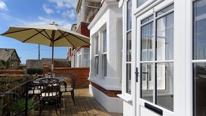 Un patio con mesa y sillas, una sombrilla y un edificio blanco con ventanas amplias.