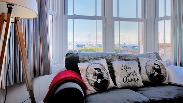 Una habitación acogedora con un ventanal grande, un sofá con cojines estampados y una lámpara.