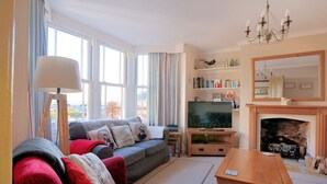 Una sala de estar con sofá, sillón, televisor, chimenea y estantería.