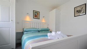 Un lit bien fait, avec une literie à rayures, une tête de lit blanche et deux lampes fixées au mur.