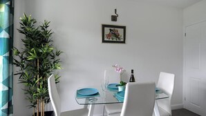 Un coin repas avec une table en verre, des chaises blanches et une plante en pot.