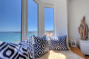 Una habitación con un amplio ventanal con vista a la playa, un tapete blanco y mullido, y cojines estampados.
