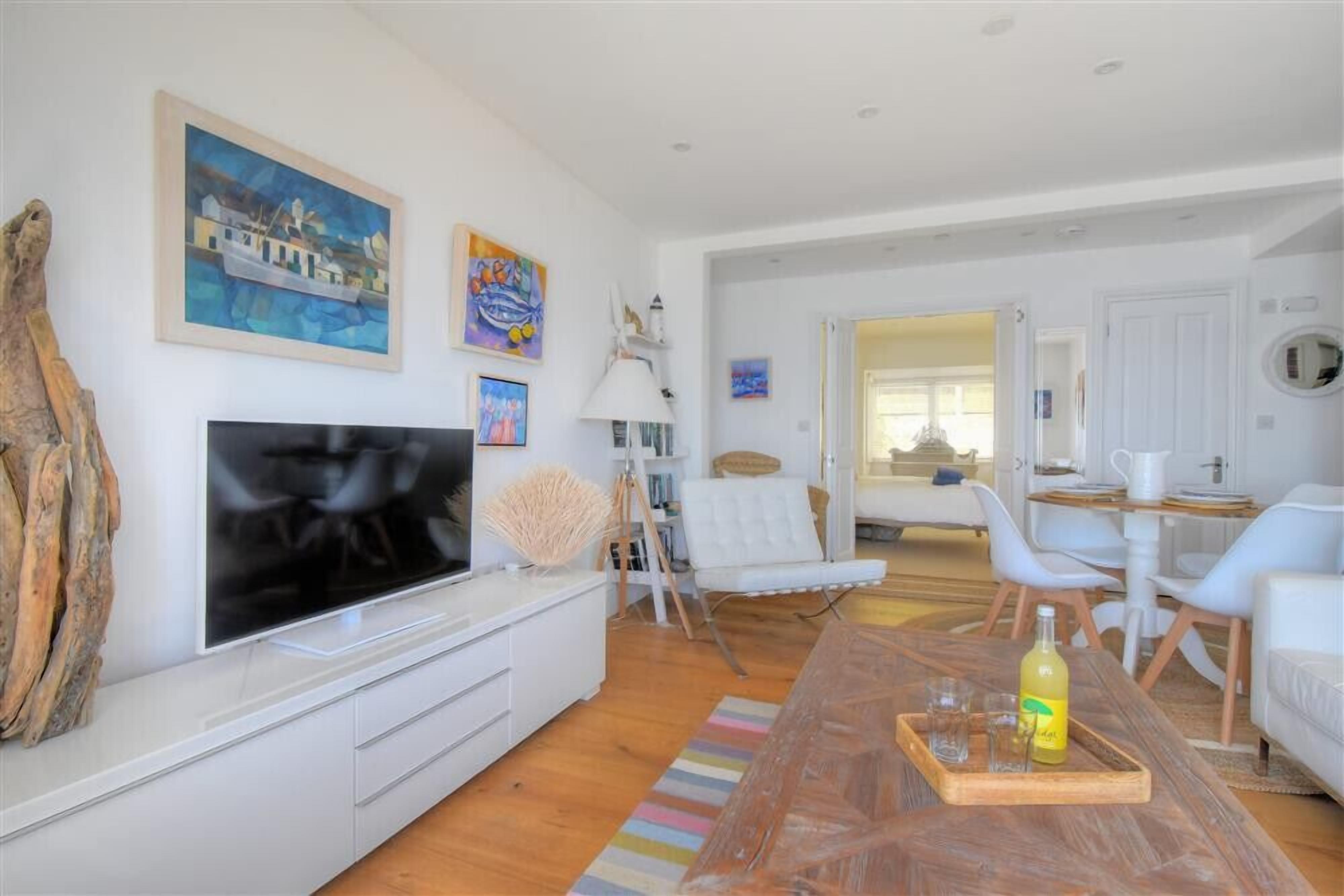 Een moderne woonkamer met een flatscreen televisie, witte meubels en kunstwerken aan de wanden.