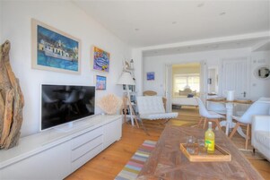 Una sala de estar moderna con un televisor de pantalla plana, muebles blancos y obras de arte en las paredes.