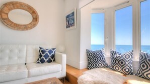 A white leather sofa with patterned cushions, a wooden coffee table, and a white furry rug. - Seahorse (Lyme Regis)