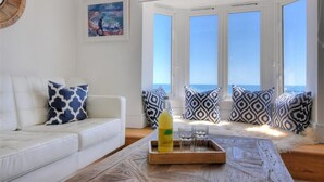 A living room with a white sofa, patterned cushions, a wooden coffee table, and a bottle of drink. - Seahorse (Lyme Regis)