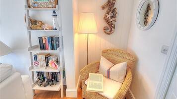 Un rincón acogedor para leer con una silla de mimbre, una estantería llena de libros, una lámpara y detalles decorativos en la pared.