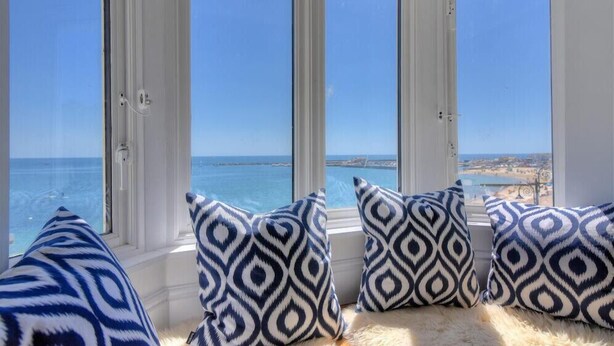 A room with a view of the sea through large windows, featuring patterned pillows and a fluffy rug. - Seahorse (Lyme Regis)