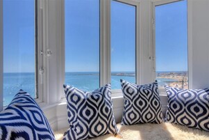 Habitación con vistas al mar a través de amplios ventanales, con cojines estampados y una alfombra mullida.