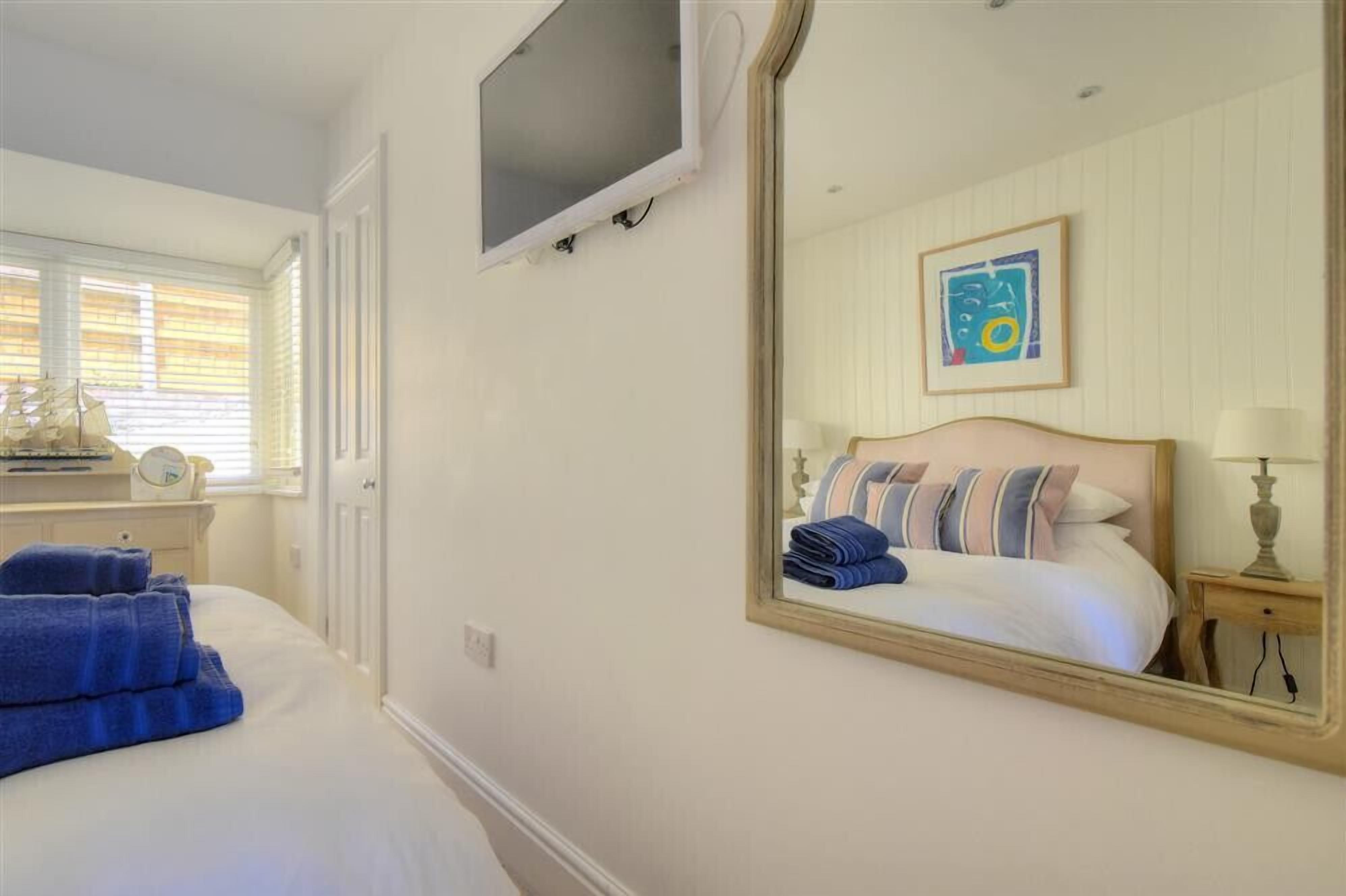 Quarto com cama, televisão fixada na parede, mesa de cabeceira com abajur e janela com persianas.