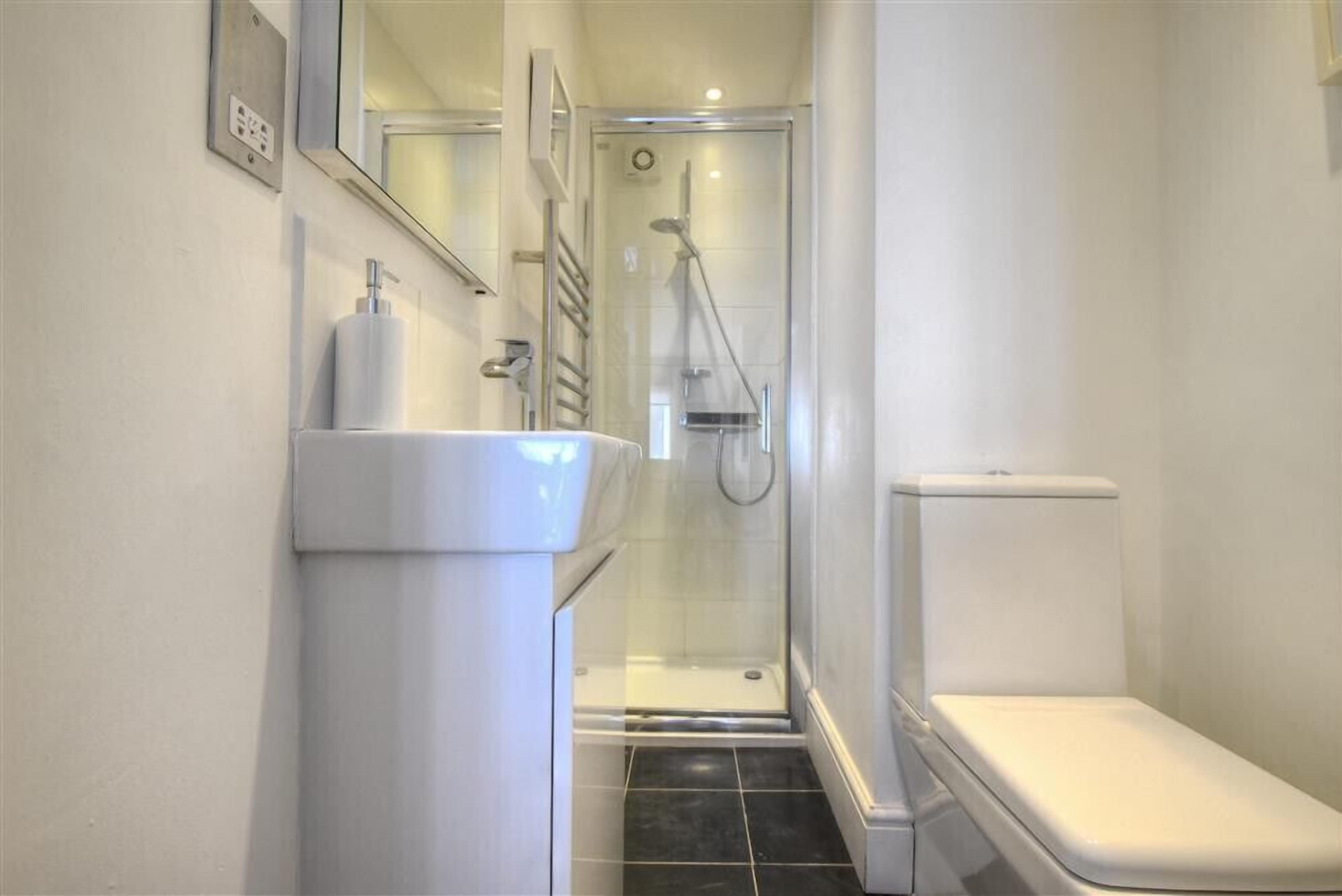 Un baño con lavamanos blanco, inodoro y ducha con mampara de vidrio.