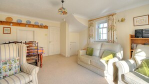 A living room with a striped sofa, a white armchair, a wooden sideboard, and a ceiling light fixture. - Blacksmiths Cottage (Lyme Regis)