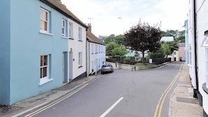 A narrow street lined with light blue and white houses, a parked car, and a tree in the background. - Bedrock (Lyme Regis)